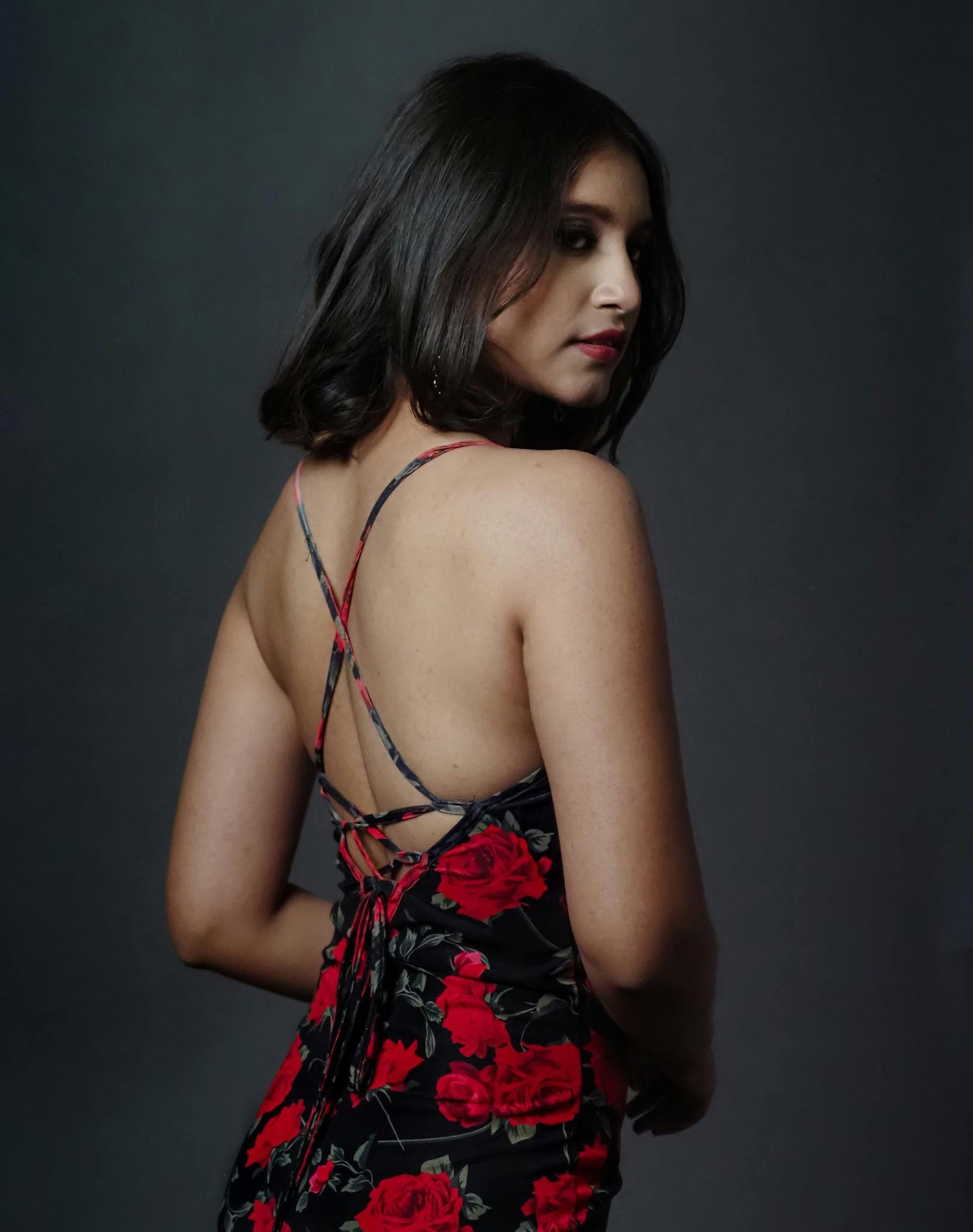 Back view of an elegant woman in a floral strappy dress in studio lighting.
