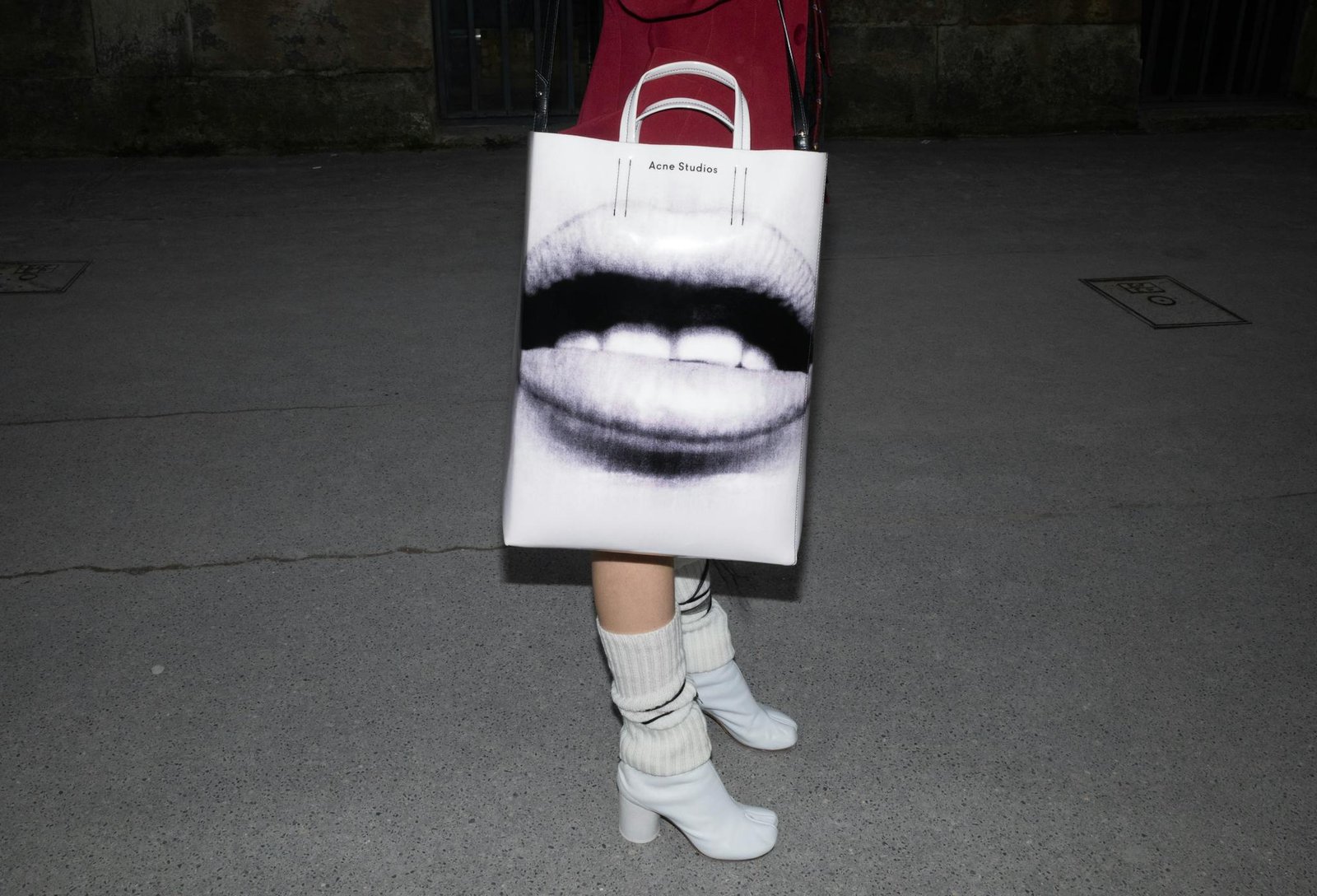Close-up of a stylish bag with art print, paired with high heels on a nighttime pavement.