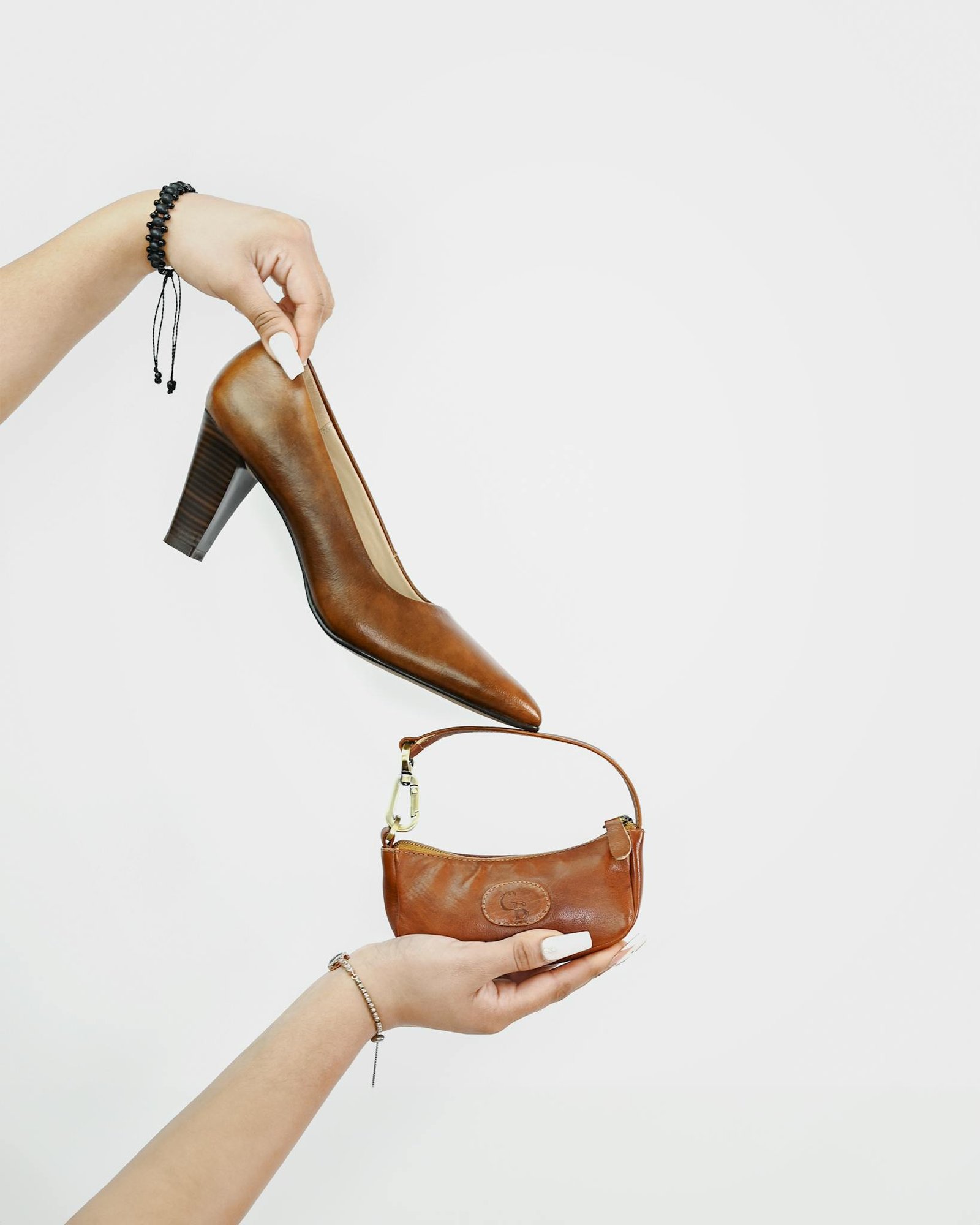 Stylish display of brown leather shoe and handbag held by hands.